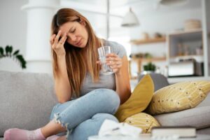 a person holds their head and a glass of water while navigating the alcohol and drug withdrawal timeline