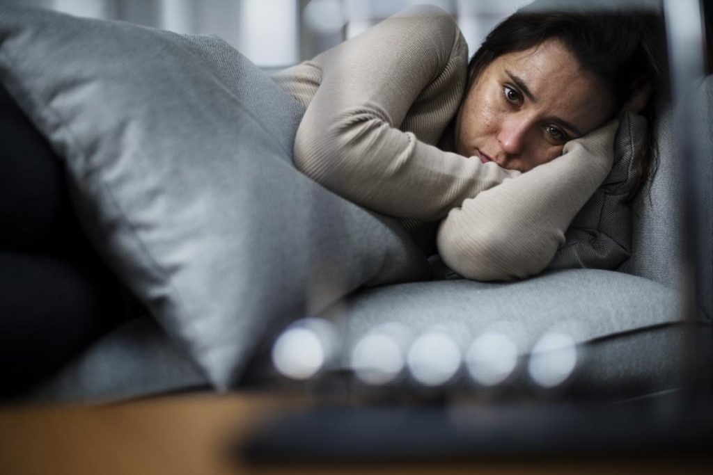 a scared woman lies in bed looking at the camera