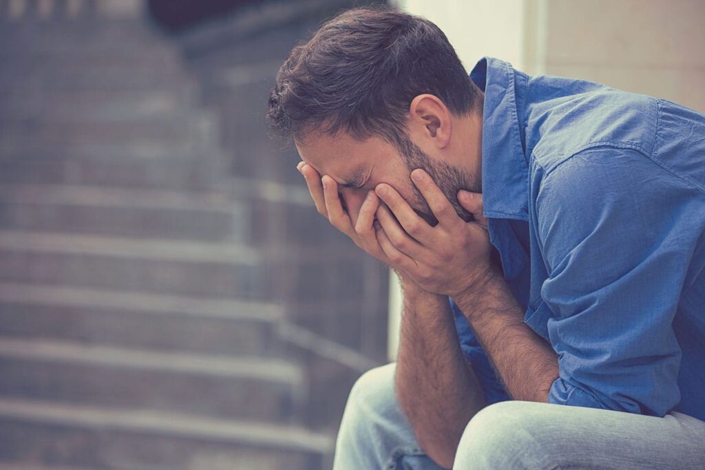 a man sits ouytside holding his head in pain as he considers addiction treatment for men