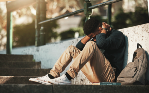 a young person sits on a sidewalk holding their head thinking of reasons why teens are using drugs