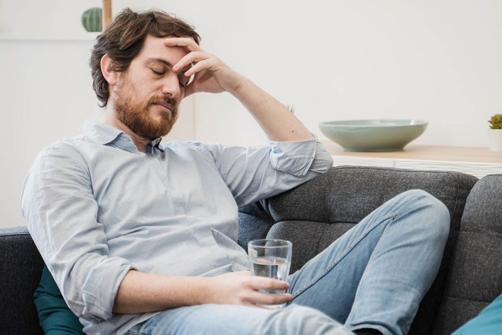 a person sits on a couch while drinking water and dealing with the signs of alcohol withdrawal