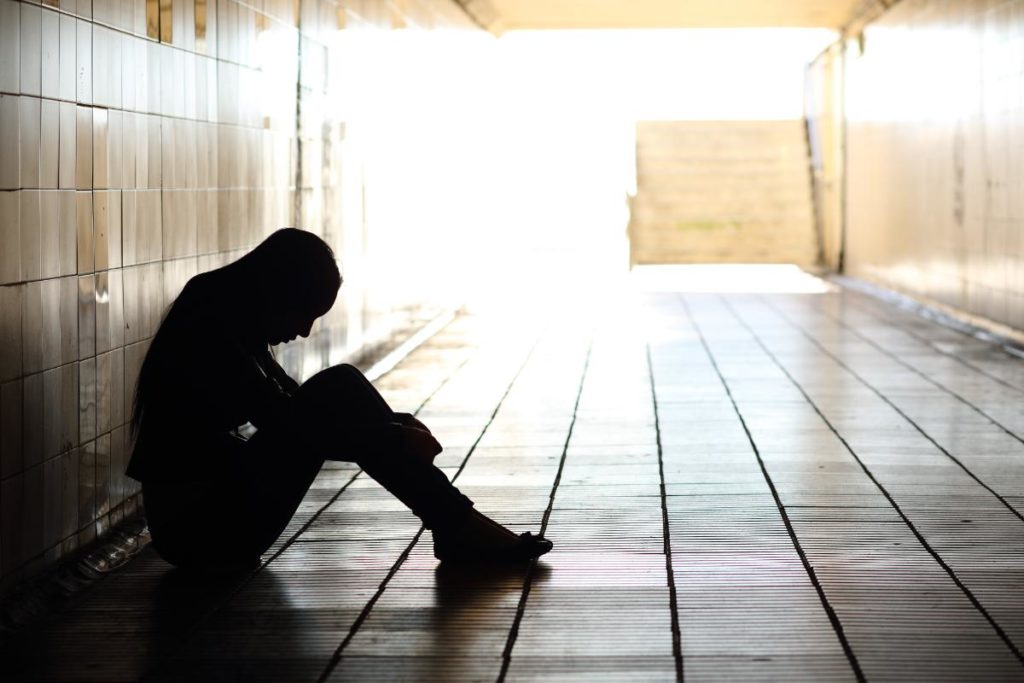 a person recognizing the signs of oxycodone abuse sits on the floor in a dark hallway