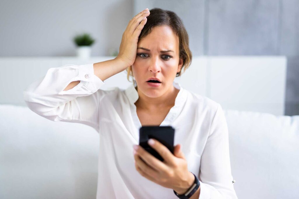 a person holds their phone and their head with different hands as they research the link between alcohol and memory