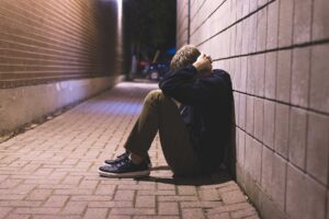 a person sits on the ground holding their head possibly wondering what is flakka?