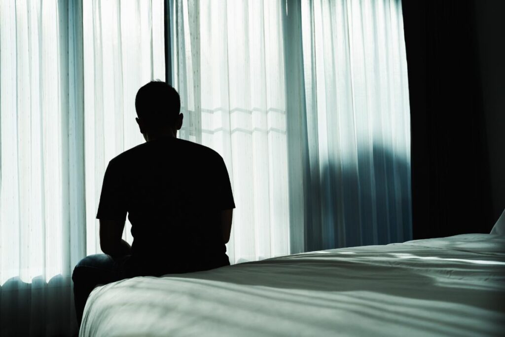 a person sits on a bed pondering if they are dealing with the side effects of lexapro