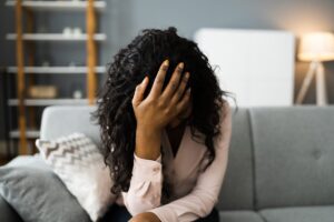 a person dealing with signs of heroin withdrawal sits on a couch holding their head