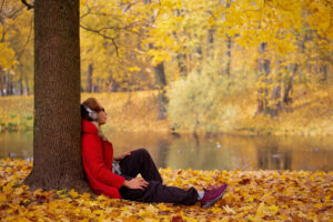 a person sits near a tree in autumn engaging in fall activities for mental health