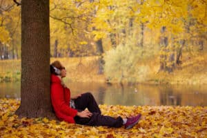 a person sits near a tree in autumn engaging in fall activities for mental health