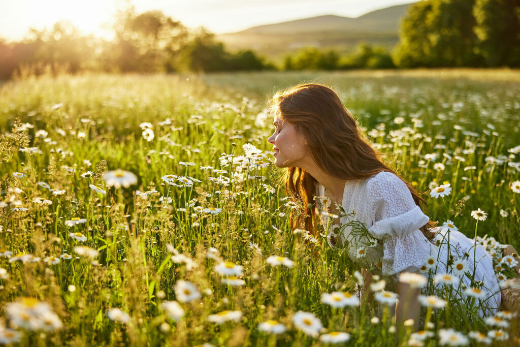 a person smells a flower in a meadow after researching how the outdoors can improve your mood